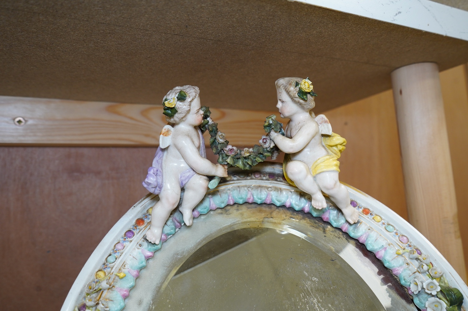 A Sitzendorf easel framed mirror, mounted with two putti holding a swag of roses, 35cm high. Condition - some damage to roses